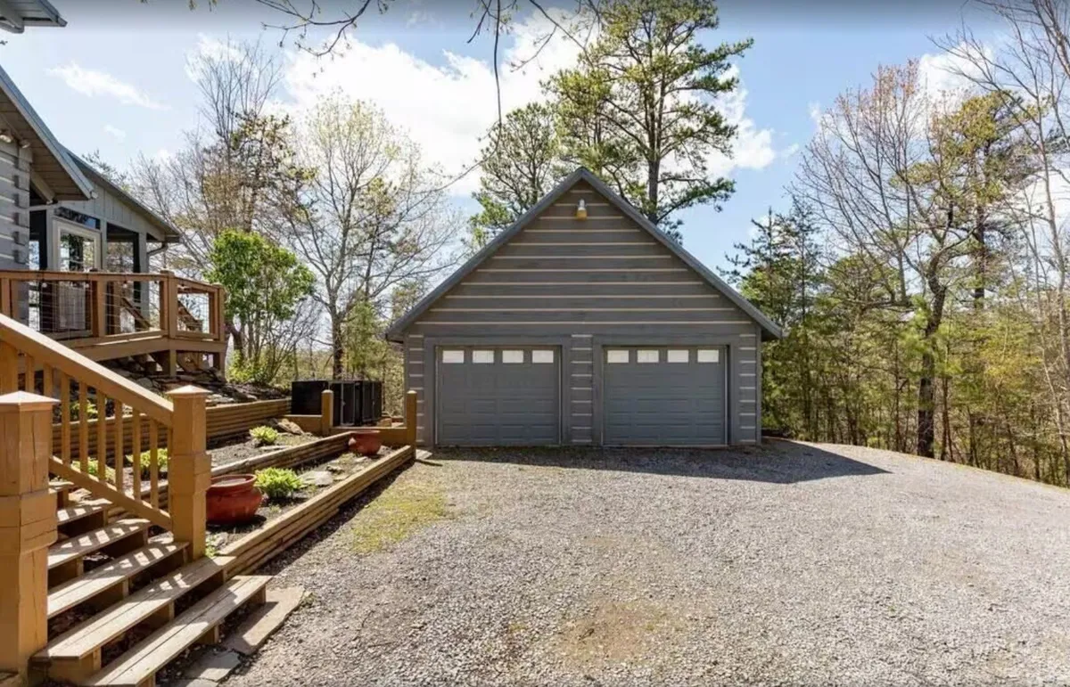 A tranquil exterior view featuring the property's garage, wooden stairs leading to the house, landscaped greenery, and a sense of openness to the outdoors. The outdoor setting is inviting, with space for parking and recreation, and hints at the spacious grounds ideal for pets to play.