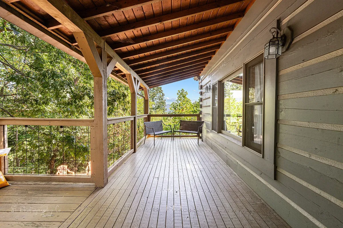 A spacious wooden deck surrounded by lush greenery, with comfortable outdoor seating arranged to take in the peaceful natural setting. The deck offers an inviting spot for relaxation and enjoyment of the outdoors, with soft, natural light filtering through the trees.