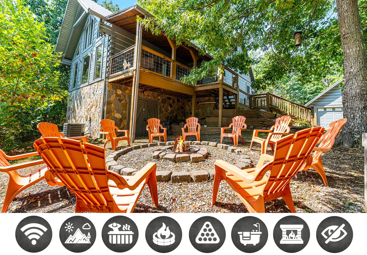 A welcoming outdoor scene featuring a cozy fire pit surrounded by vibrant orange chairs set on a stone patio, backed by a rustic wooden deck and framed by natural mountain greenery—perfect for gatherings and relaxation.