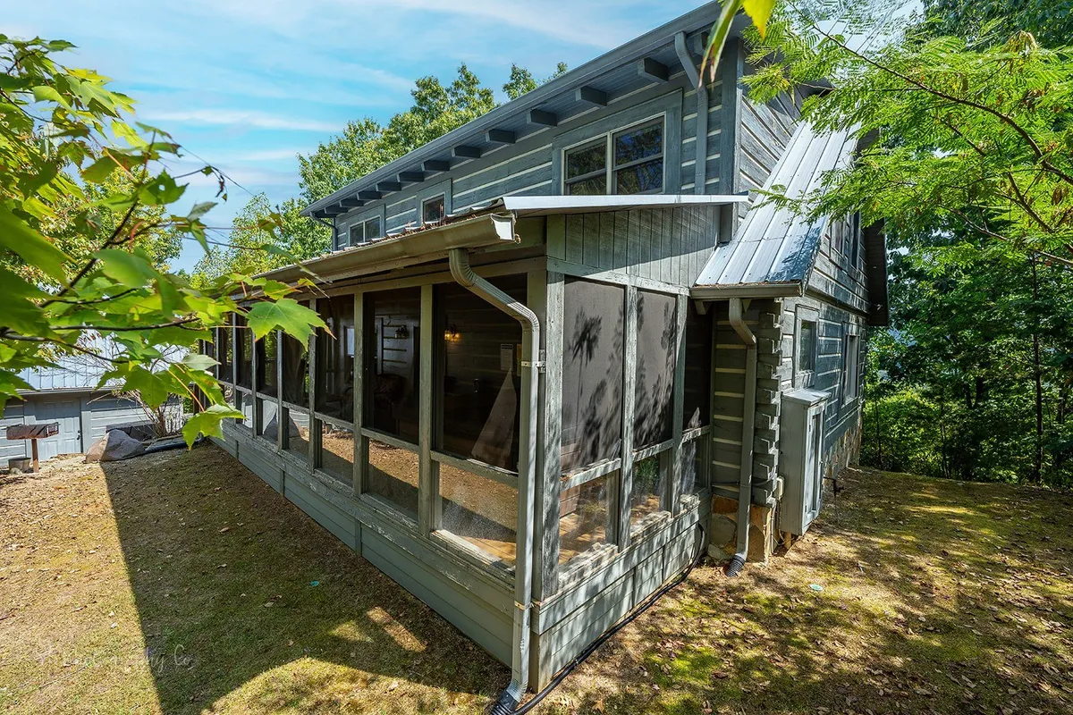An inviting exterior scene featuring a screened porch with wooden siding, embraced by surrounding trees, hinting at peaceful mornings with sunrise coffee or evenings spent stargazing close to nature.
