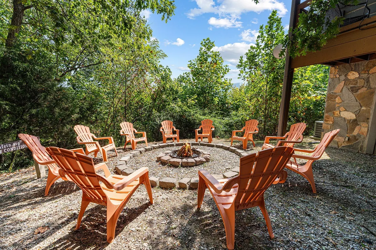 A cozy outdoor fire pit surrounded by Adirondack chairs nestled among trees, offering a welcoming space for guests to gather, share stories, or make s'mores under the night sky.