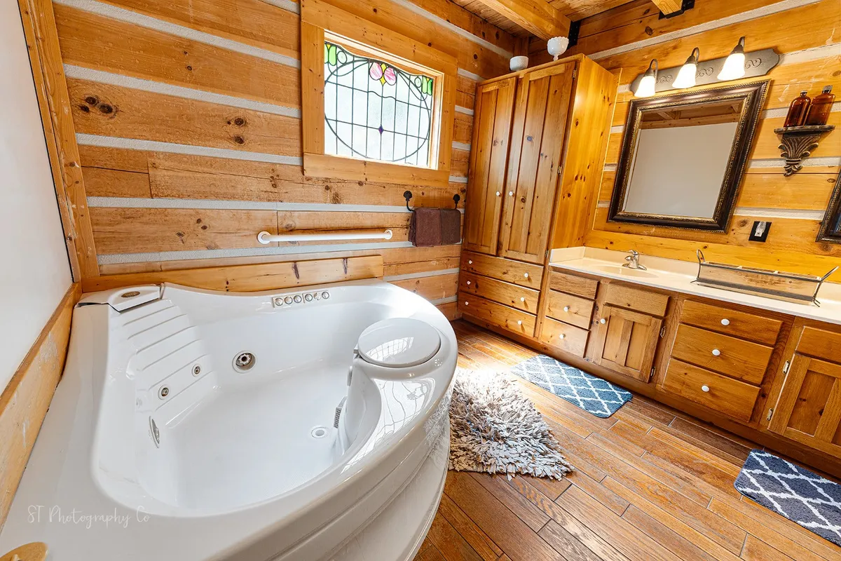 A luxurious bathroom featuring a large jacuzzi tub, stained glass window, wooden cabinetry, and a large mirror. The space exudes a spa-like tranquility, offering a place for relaxation and rejuvenation after a day of adventure.