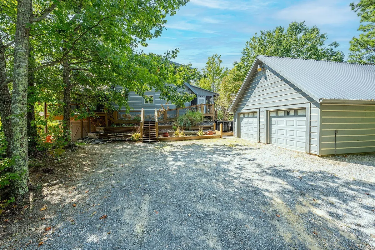 A wide exterior view of the Family Adventure Lodge, showcasing the house, garage, staircase, and well-maintained landscaping. The scene evokes a welcoming vibe, perfect for group arrivals and outdoor activities. The home's spacious layout is visible, emphasizing its capacity for large gatherings.