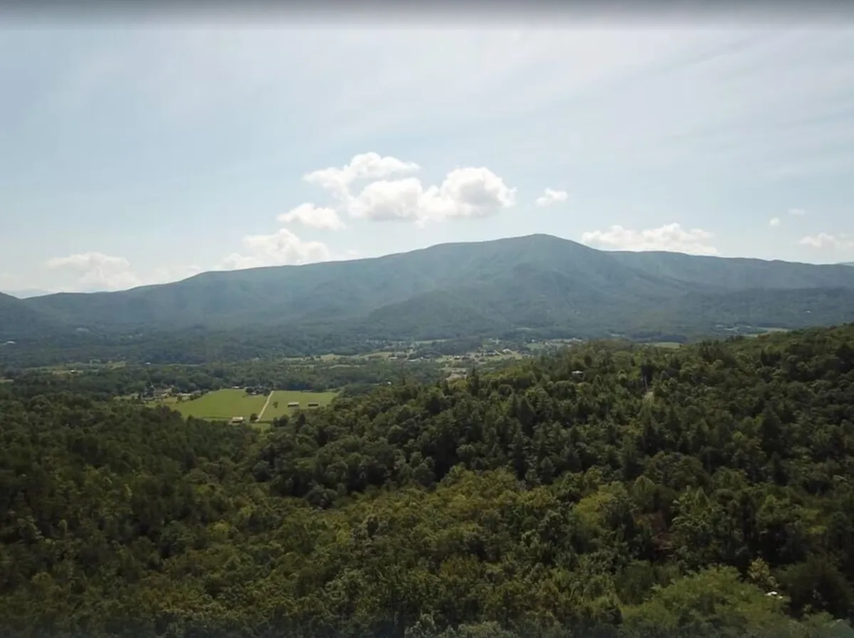 A panoramic vista of the Smoky Mountains, with lush greenery, open fields, and dramatic clouds overhead. The landscape is iconic of the area, evoking the adventure, beauty, and sense of exploration that attract visitors to the region.