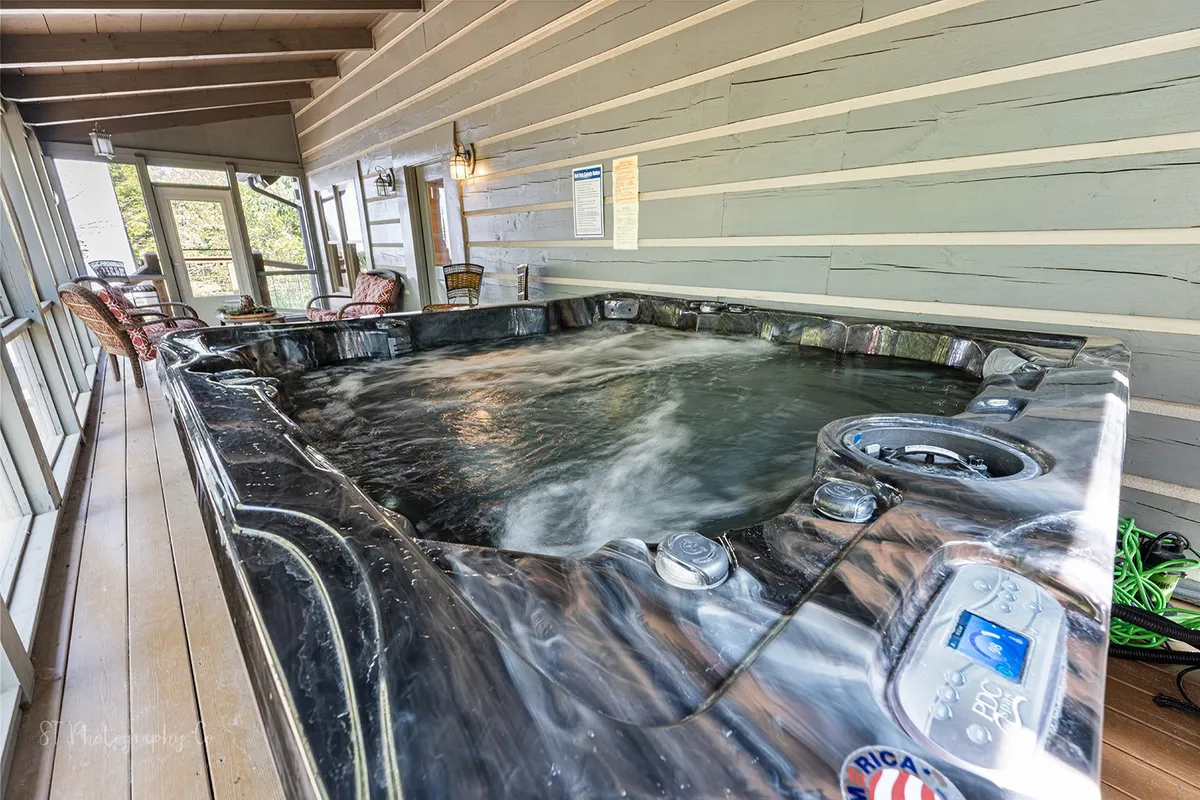 A tranquil interior space featuring a hot tub on a screened-in wooden deck, surrounded by comfortable seating. The warm wood details blend indoor comfort with outdoor ambiance, inviting guests to relax, socialize, and soak in the mountain air.
