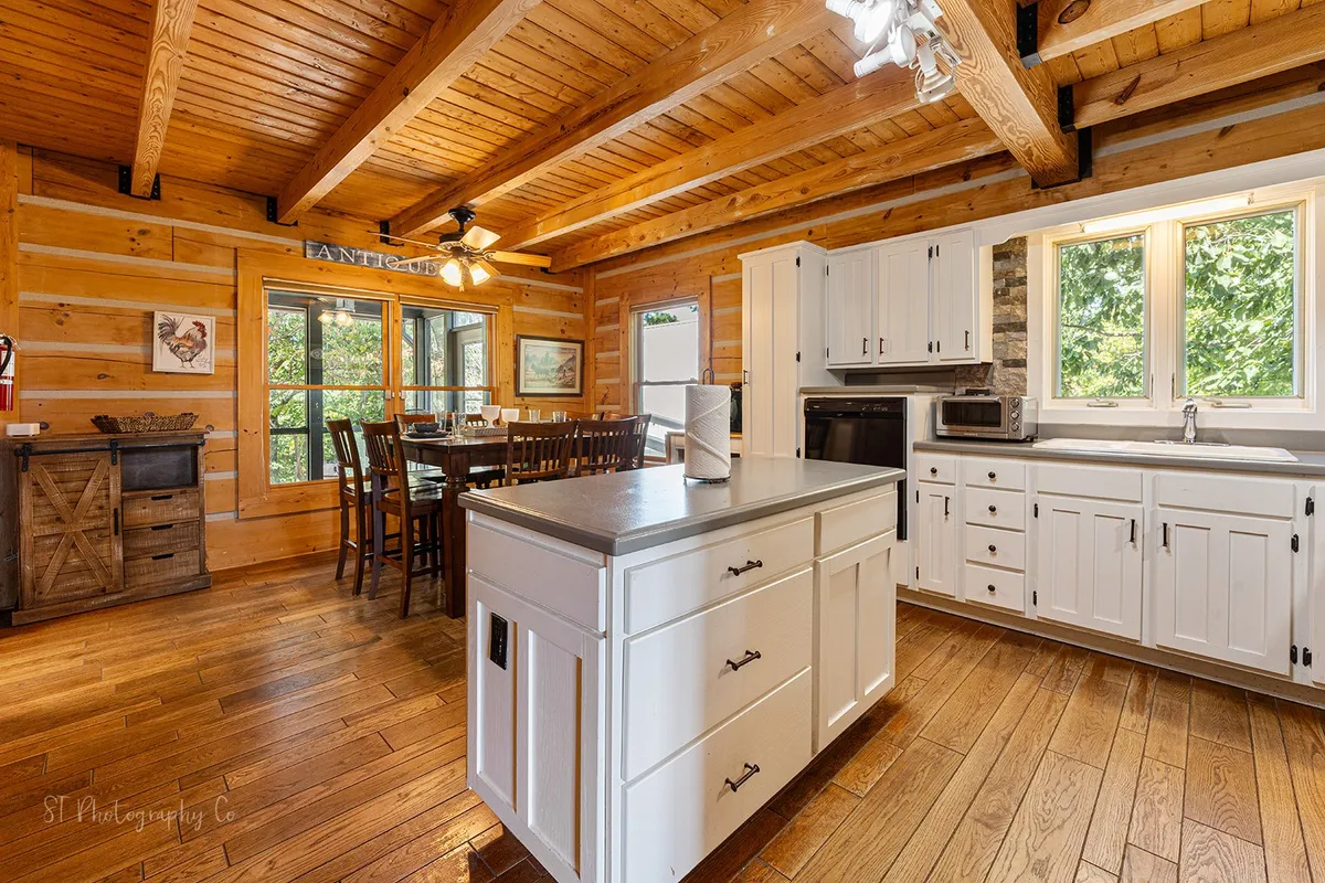 An open-concept kitchen and dining area with a central kitchen island and a large dining table positioned by windows that offer scenic views. The space is cozy, functional, and designed for socializing and group meals.